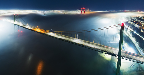 A night time aerial drone view of the MacKay bridge spanning Halifax harbour. A fog bank enshrouds the area.