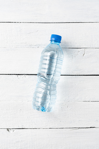 Overhead shot of plastic bottle with water on white wooden table. Flat lay