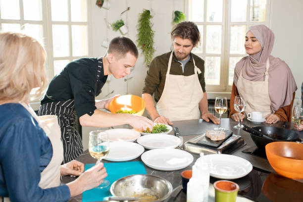 istock Young cooking coach in apron bending over large kitchen table and taking fresh ruccola for salad 1309278239