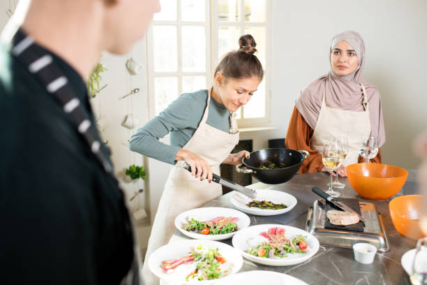 istock Young female with frying pan bending over large kitchen table while putting vegetable stew on plate 1309278253