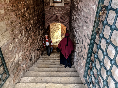 Istanbul, Turkey - October 29, 2019: Two Turkish persons walking towards each other in a narrow ancient stone Passageway in Suleymaniye Mosque in Istanbul. Woman goes down the stairs, and the man goes up