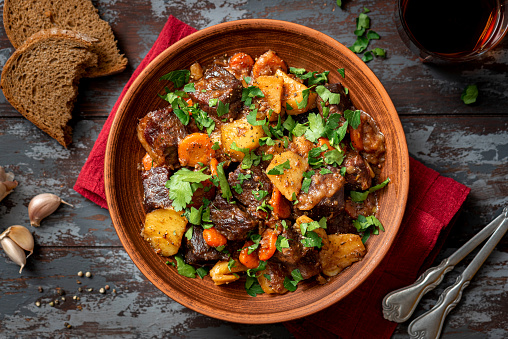 Goulash. Beef stew with potatoes, onions, carrots and spices in a ceramic plate on a dark wooden table top view. Rustic style. Stewed meat with vegetables.