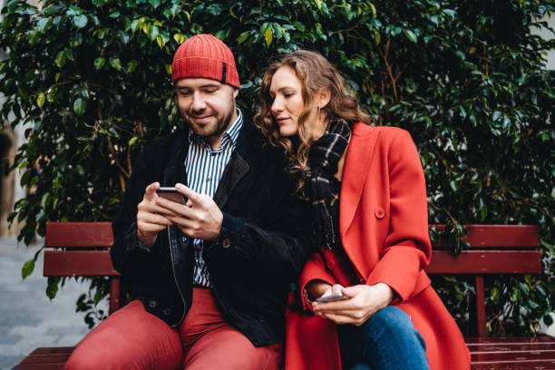 istock Smiling couple sitting outdoors and using mobile phone 1309292624