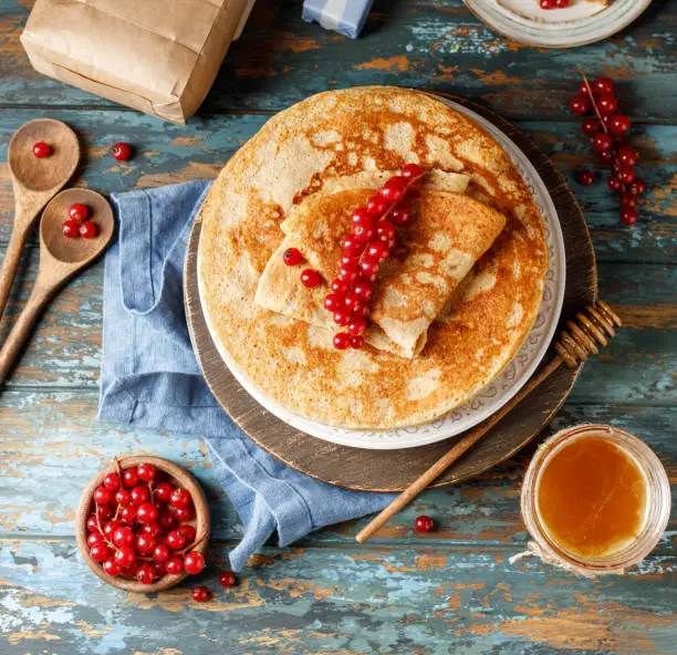 Pancakes with honey and red currants on white plate. Maslenitsa