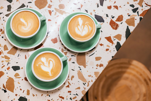 Top view of three cups of coffee with beautiful latte art in a green cup on a stone table background.