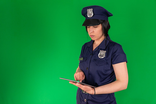 Studio shoot of a dedicated policewoman in uniform, checking the database on her tablet computer while standing in front of a green background