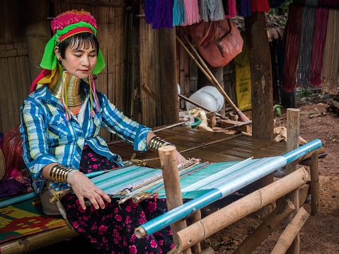 Chiang Mai, Thailand - January 4, 2017: Karen long neck woman wearing traditional brass rings and weaving a shawl in a hill tribe village near Chiang Mai in Northern Thailand.