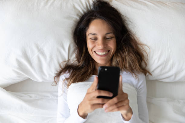 istock Top view smiling woman using phone, resting in bed 1309312515