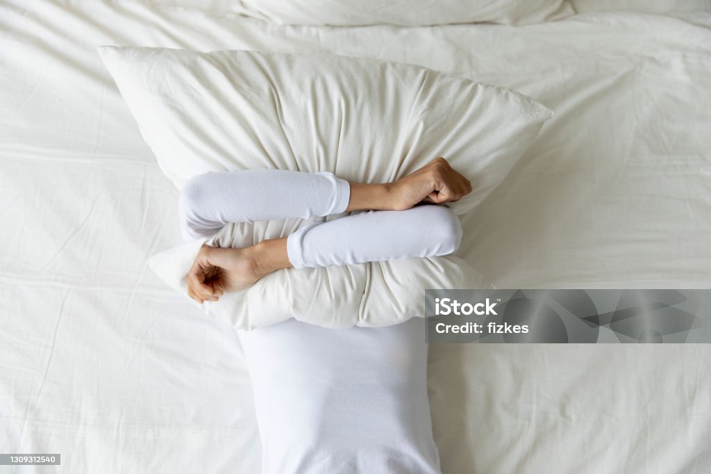 Top view depressed woman covering face with pillow, lying alone Top view depressed woman covering face with pillow, lying on bed at home alone, frustrated unhappy young female suffering from insomnia, mental or relationship problems, break up or divorce Insomnia Stock Photo