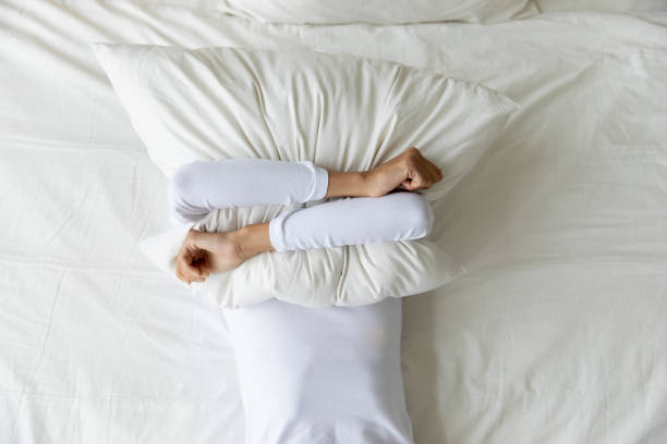 Top view depressed woman covering face with pillow, lying alone Top view depressed woman covering face with pillow, lying on bed at home alone, frustrated unhappy young female suffering from insomnia, mental or relationship problems, break up or divorce insomnia photos stock pictures, royalty-free photos & images