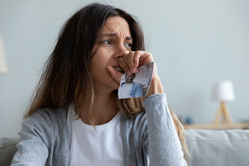 Close up crying woman holding torn picture of husband, break up with boyfriend or divorce, upset frustrated young female suffering from bad relationship problem, feeling lonely and depressed