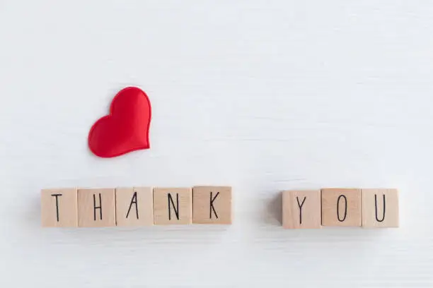 The word thank you on wooden cubes and a red heart on a light background with space for your text.