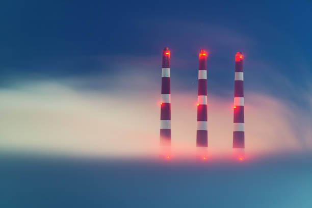 The silhouettes of the steaming pipes of thermal power station on the background of scarlet sunrise or sunrise. The cloudy sky cloured in red, orange, rose, scarlet, crimson, purple, violet and blue