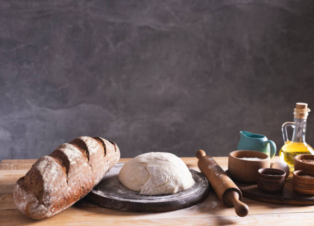 Dough and bakery ingredients at pizza board for homemade bread cooking or baking on table. Food set at wooden tabletop Bread and bakery ingredients for homemade cooking or baking on table. Bread set at wooden tabletop near wall background texture with copy space. Front view of bakery concept best bread proofing stock pictures, royalty-free photos & images