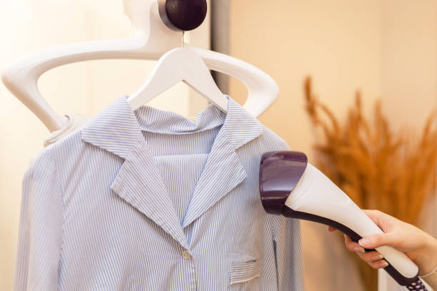istock Using steaming iron to ironing shirt in laundry room. Doing stream vapor iron for press clothes in hand. selective focus 1309316578