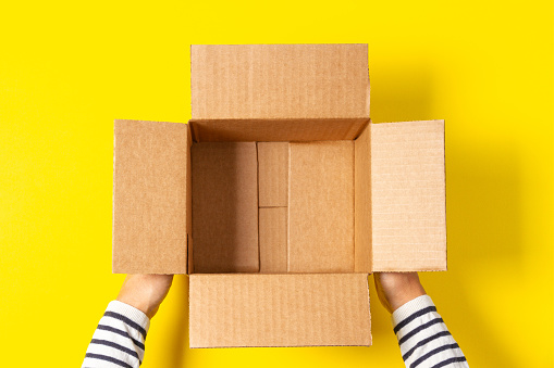 Female hands with empty open cardboard boxes on yellow background. Top view.