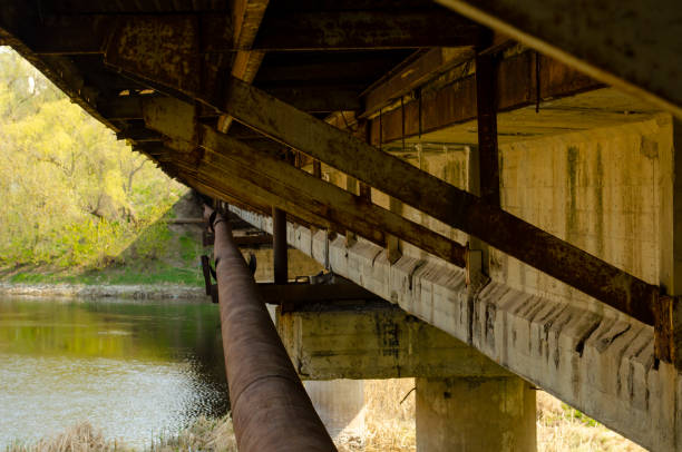 istock Reinforced concrete bridge dilapidated pillars. Overpass seen from below showing support beams. Bridge over river 1309320696