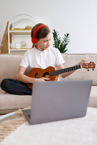 istock boy tunes guitar, before playing guitar, home teaching music 1309326842