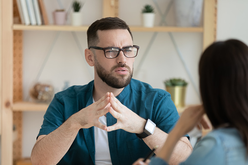 Unhappy young Caucasian man worker talk with female colleague thinking doubting at office meeting. Frustrated confused male employee brainstorm with coworker, solve problem at briefing.