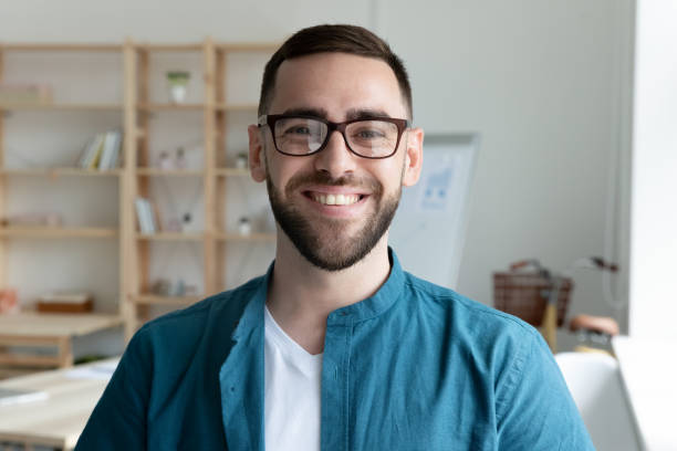 Headshot portrait of smiling male employee in office Close up headshot portrait of smiling young Caucasian businessman in glasses posing in office. Profile picture of happy millennial male employee or worker in eyewear at workplace. Employment concept. bossy photos stock pictures, royalty-free photos & images