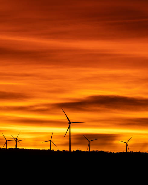 wind turbine silhouettes in a cloudy sunset silhouettes of wind turbines in a cloudy, orange sunset landscape alternative energy scenics farm stock pictures, royalty-free photos & images