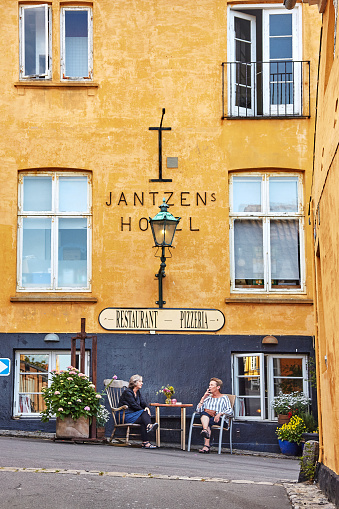 Gudhjem, Bornholm island, Denmark - June 29, 2019. Two women sitting by the table in front of the Jantzens Hotel founded in 1872 which makes it the oldest hotel in Gudhjem.