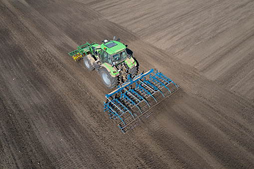 Aerial view of a modern tractor with front and rear mounted cultivator working in field.