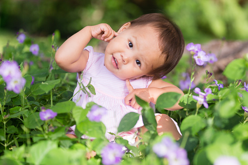 Adorable little asian female toddler joyfully playing in the beautiful spring flower garden.