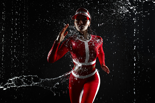 Beautiful young girl in sportswear in aqua studio. Drops of water spread about her fitness body. The perfect figure on the background of water splashes. Bad weather for sport