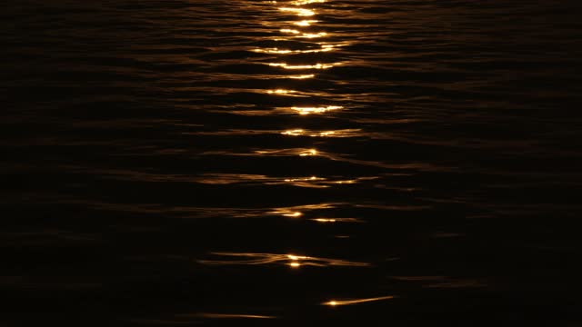 Narrow beaming sunlight path reflection on pitch black water