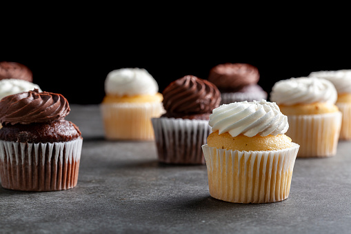 Side view image of vanilla and chocoloate cupcakes on dark stone countertop against black background. Concept for parties, celebration and late night snack