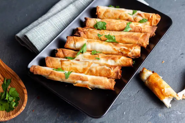 Traditional Turkish sigara boregi: some sort of deep fried phyllo dough pasty rolls with cheese or meat inside. Served on flat plate on stone. with parsley leaves for seasoning and decoration