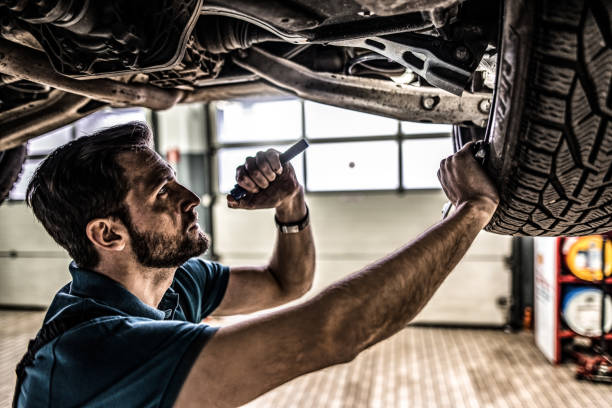 Mechanic examining a car from beneath at repair shop. Young auto mechanic examining and fixing a car at auto mechanic shop. shock absorber stock pictures, royalty-free photos & images