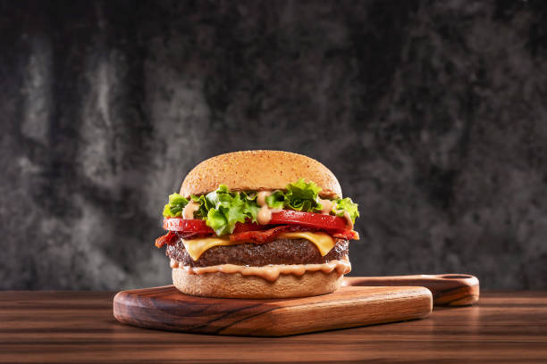 sajtburger paradicsommal és salátával fadeszkán - hamburger témájú stock jellegű vizuális alkotások, jogdíjmentes fotók és képek