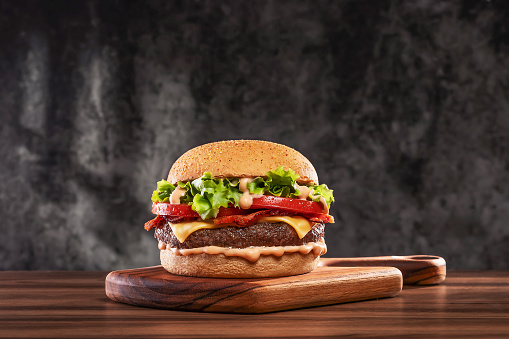Cheeseburger with tomato and lettuce on wooden plank