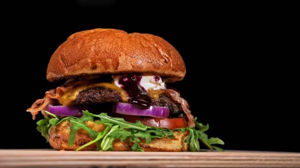 istock Craft burger is cooking on black background. Consist: sauce, arugula, tomato, onion, bacon, currant sauce, ricotta cheese, air bun and marble meat. 1309359403