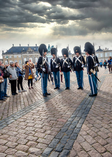 Copenhagen, Denmark - April 28, 2024: Two Royal Guards with rifles stand watch at Amalienborg Palace. The palace square and surrounding buildings create a historic backdrop.