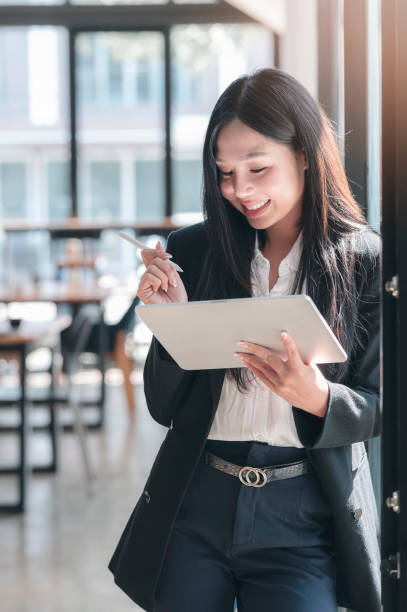 istock Young asian businesswoman using stylus pen working on tablet with happiness while standing in office room. 1309367842