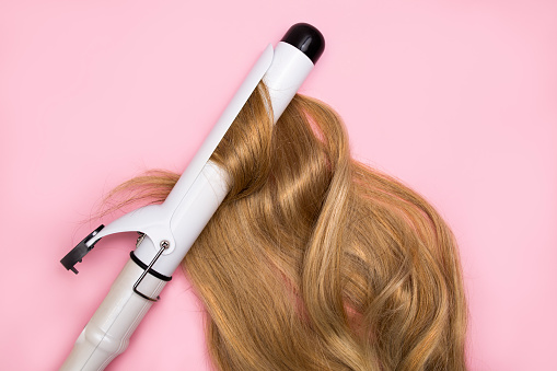 Rizar el cabello rubio sobre un rizador de gran diámetro sobre un fondo rosa. Concepto de salud del cabello, daño por el peinado del cabello caliente. photo