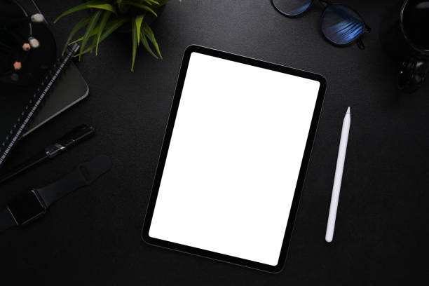 istock Mock up image of digital tablet with blank screen, stylus pen, smart watch, glasses and notebook on modern dark workplace. 1309370255