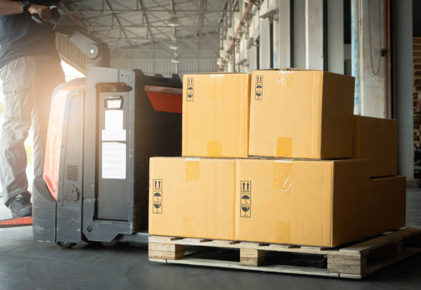 istock Cardboard boxes on Wooden Pallet with Worker Driving Electric Forklift Pallet Jack Unloading at The Warehouse. Storage Warehouse. Cargo Shipment Boxes. 1309373481