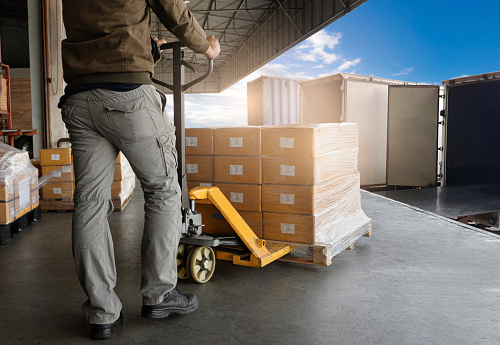 Warehouse Worker Unloading Shipment Boxes into Cargo Container Truck. Cargo Trailer Truck Parked Loading at Dock Warehouse. Delivery Service. Shipping Warehouse Logistics. Freight Truck Transportation.