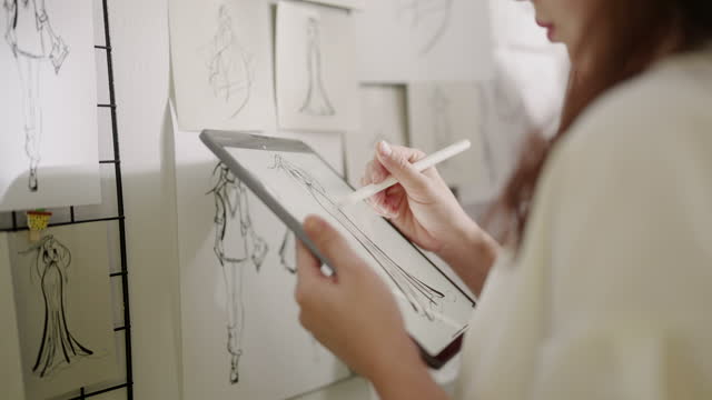 USA,Japan Fashion Designer Sketching Clothing on her Digital tablet with Sketch paper on the wall