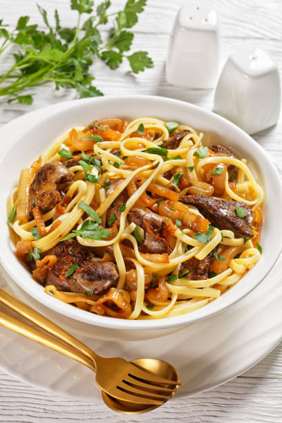 istock pasta linguine with fried chicken liver, caramelized onion and parsley in a white bowl, verticall view from above, Italian cuisine 1309375196