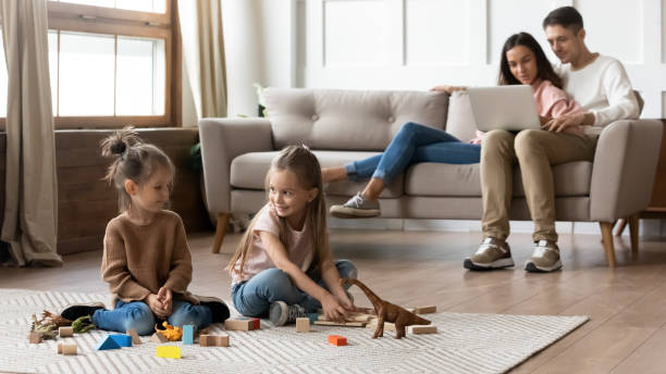 istock Couple rest on sofa with laptop while daughters play toys 1309383525