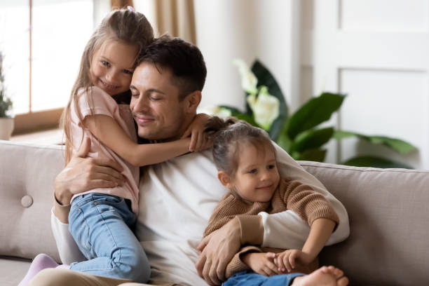 istock Dad hug two cute daughters resting together on couch 1309383542
