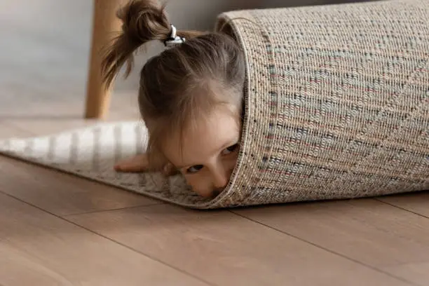 Photo of Playful girl wrapped in carpet lying on floor at home