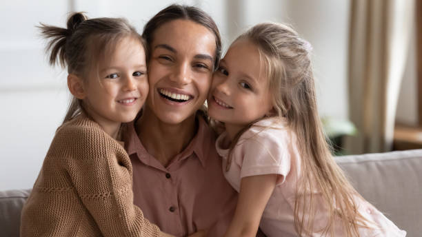 istock Little daughters hug mom smiling looking at camera 1309383563