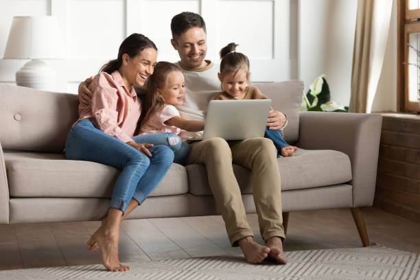 istock Family with daughters relaxing on sofa using laptop watching cartoons 1309383566