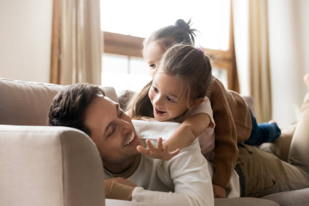 istock Happy father lies on couch with two little daughters 1309383574